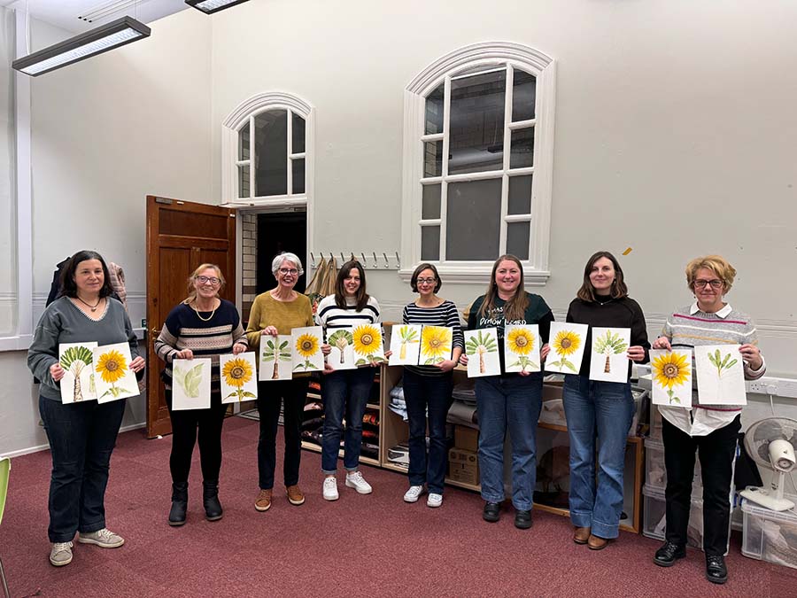 Group of women holding sunflower paintings in a room with white walls and wooden doors.